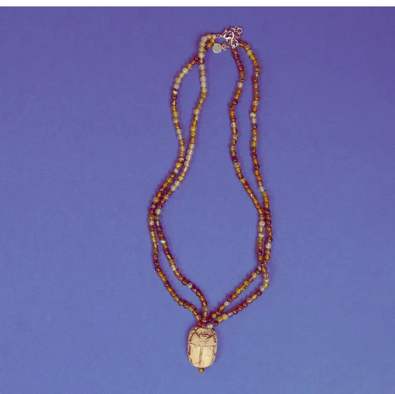 Collier scarabée égyptien en stéatite et perles d'agate verte sur fond bleu