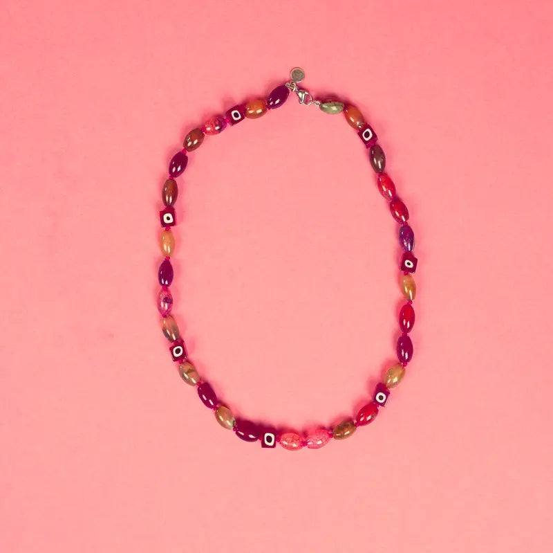 Détail du collier Hob et ses perles carrées rouges sur fond rose