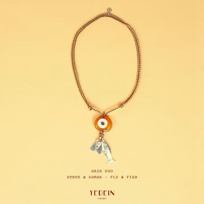 Collier Abir Duo avec un œil ambre et deux charms Samak et Deben sur fond beige
