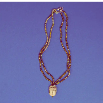 Collier scarabée égyptien en stéatite et perles d'agate verte sur fond bleu
