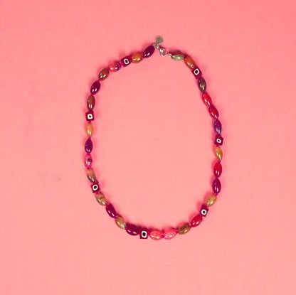 Détail du collier Hob et ses perles carrées rouges sur fond rose